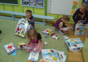 Dzieci siedzą na dywanie i rozpakowują otrzymane prezenty